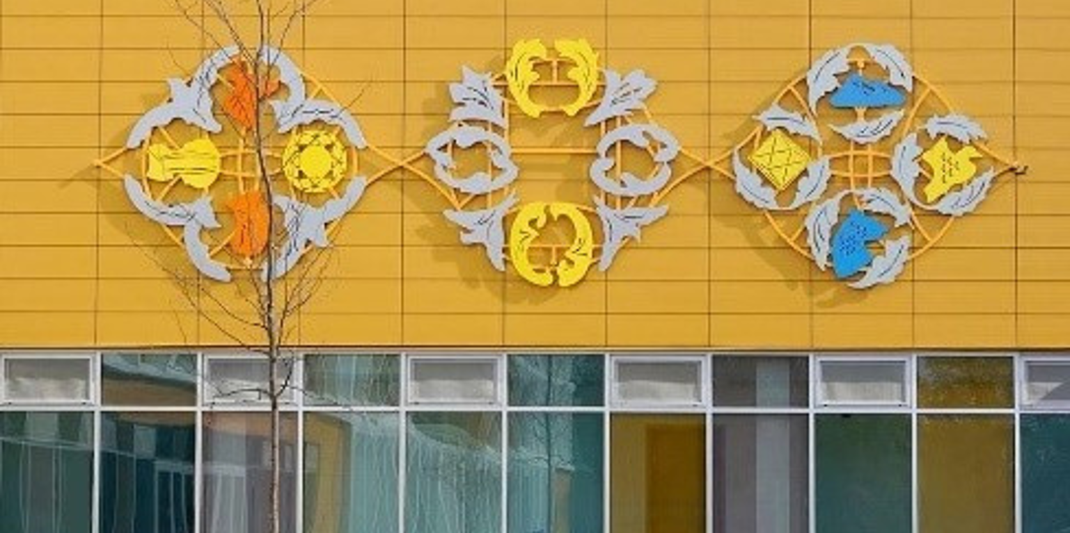 Oeuvre d'art accrochée sur la facade jaune d'une école. Ressemble à tes fleurs ou une mosaique.